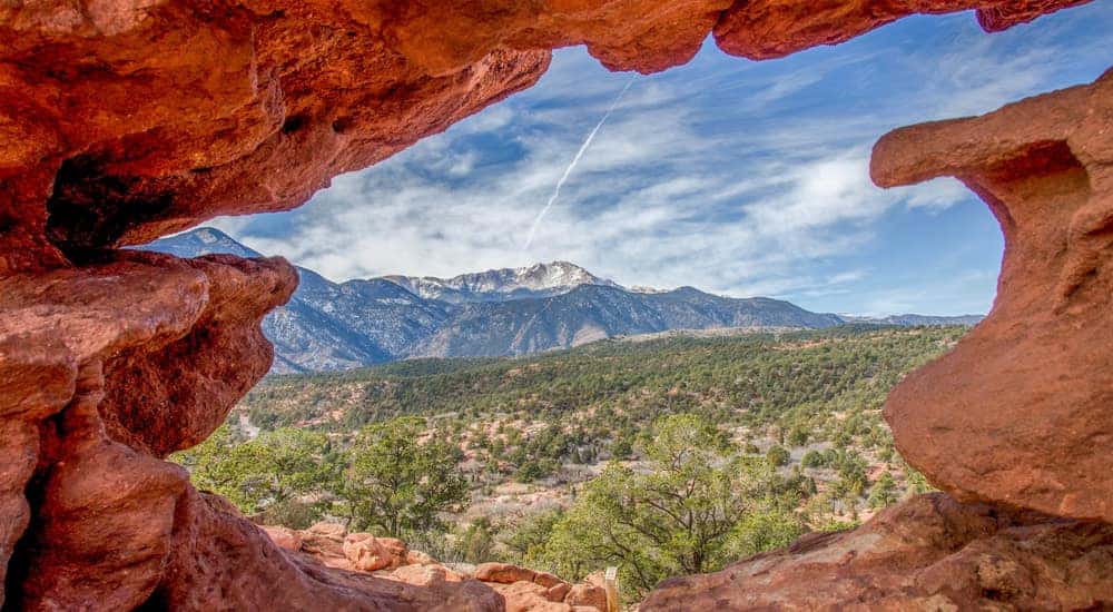 Red rock wall with a hole in the middle revealing tall Colorado mountains and trees
