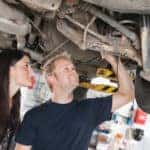 Two people are shown looking at the suspension of a car on a lift.