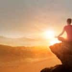 Woman sitting cross-legged on top of a mountain in front of a sunset