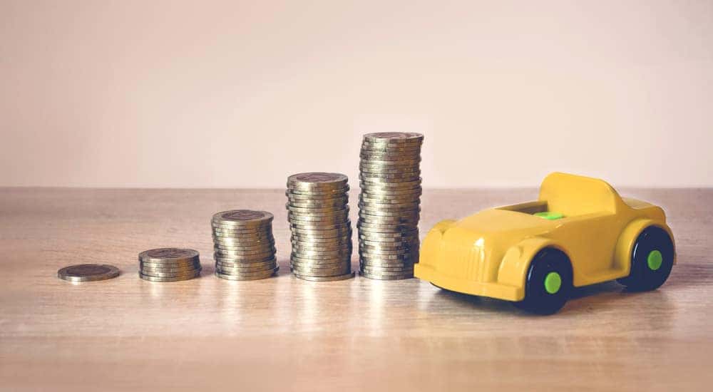 Six stacks of change, each progressively taller, next to a yellow toy car on a light brown table