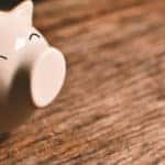 A pink piggybank with a happy expression is sitting on a dark brown wooden table.