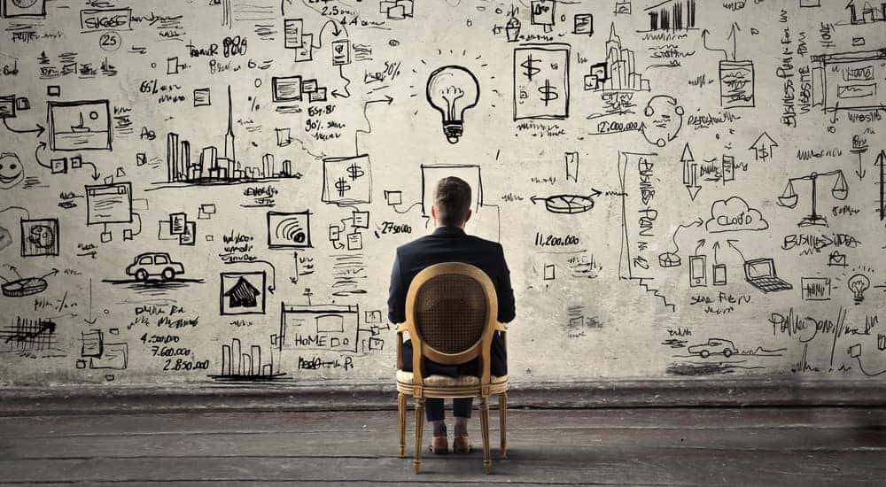 Man sitting in a brown chair facing a wall covered in writing and drawings that indicate planning and strategy