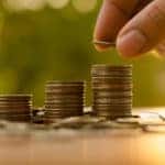 Three stacks of coins around a pile of coins with a hand contributing to the third one