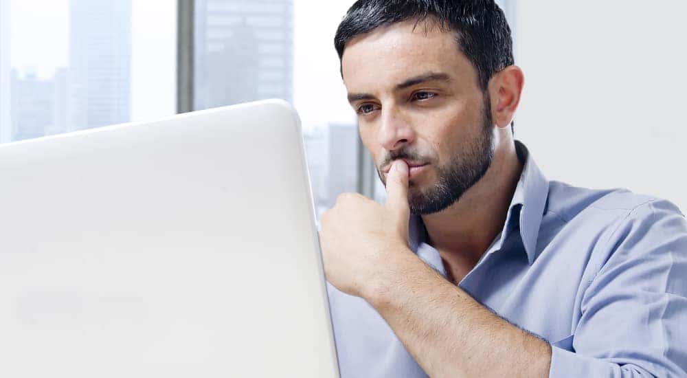 Man with facial hair in a blue shirt sitting at a desk with a laptop