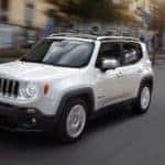 A Certified Pre-Owned white 2018Jeep Renegade is driving downtown.