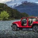 A red 2019 Jeep Wrangler has the top and doors of and is parked on rocky ground with mountains in the distance. Check one out at a Jeep dealership in Colorado Springs.