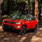A red Jeep Compass, popular among used SUVs for sale, is driving in the woods near Colorado Springs, CO.