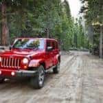 A red 2017 Jeep Wrangler, which is popular among used car in Colorado Springs, CO, is driving on a dirt backroad.