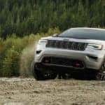 A silver 2019 Jeep Grand Cherokee is driving up a hill while making dirt flying.