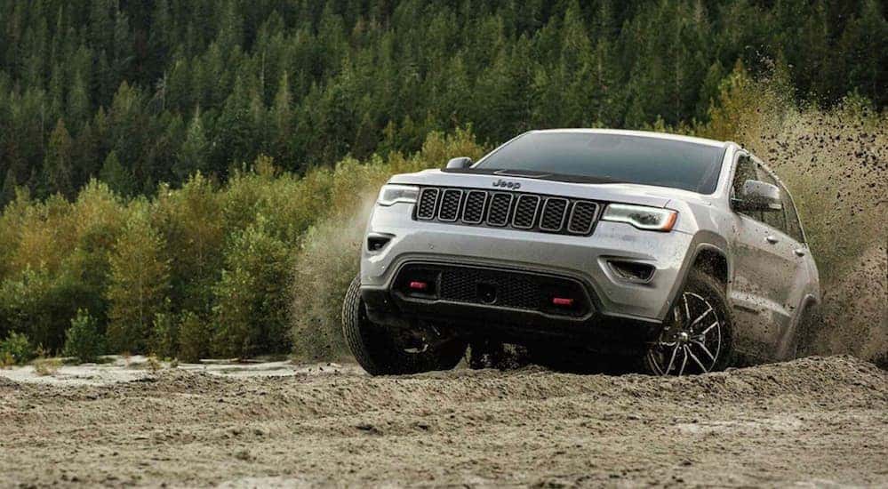 A silver 2019 Jeep Grand Cherokee is driving up a hill while making dirt fly.