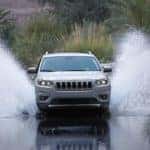 A grey 2020 Jeep Cherokee, which is a popular option among Jeep models in Colorado Springs, CO, is driving through a large puddle.