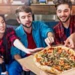 Three smiling friends are enjoying pizza at a Colorado Springs, CO, pizza restaurant.