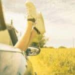A woman has her feet out of her car on a summer day.