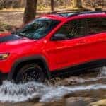 A red 2020 Jeep Cherokee Trailhawk, which is popular among Jeeps for sale in Colorado Springs, CO, is off-roading through water.
