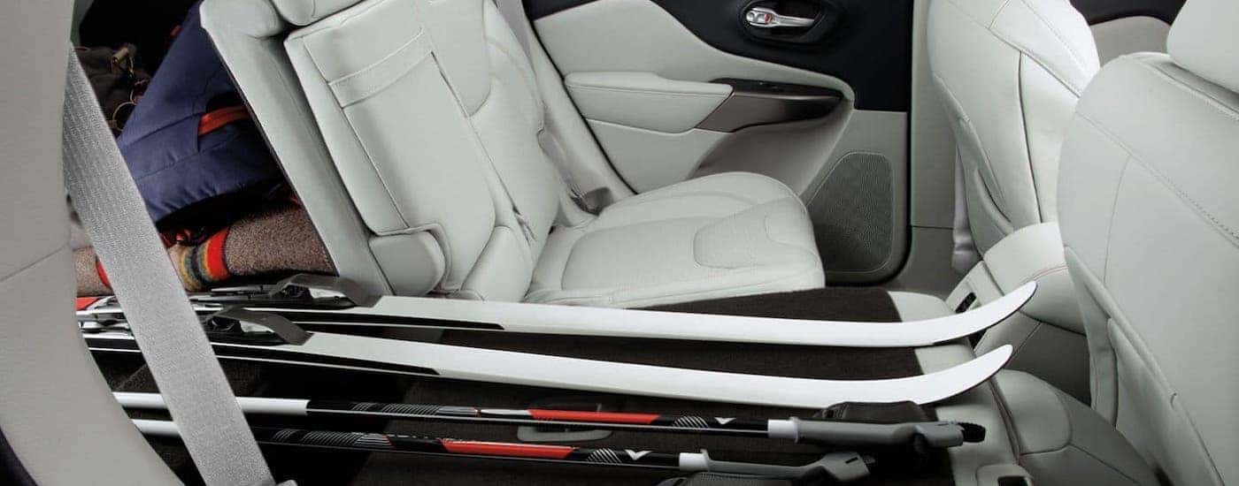 The white interior of a 2019 used Jeep Cherokee in Colorado Springs is shown with skis in the cargo area and back seat.