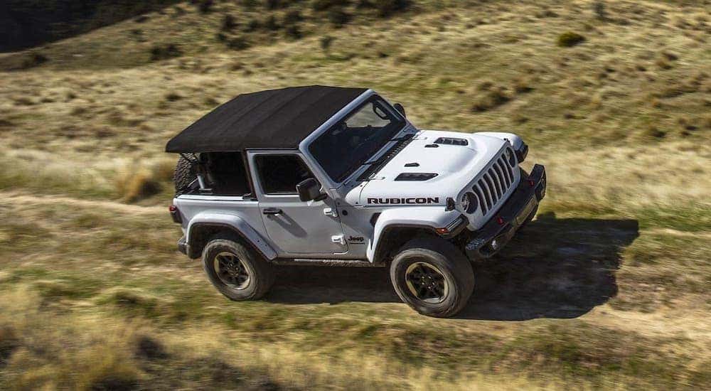 A white Certified Pre-Owned 2019 Jeep Wrangler with a soft top is driving in a field near Colorado Springs.