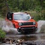 An orange 2020 Jeep Renegade Trailhawk is driving through a river.