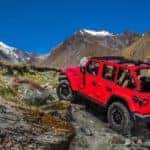 A red 2021 Jeep Wrangler Unlimited with no roof is climbing up rocks on a mountain.