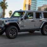 A gray 2021 Jeep Wrangler 4xe is driving on a city street.