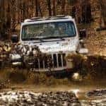 A white 2021 Jeep Wrangler is shown from the front driving through a mud puddle in the woods near Colorado Springs.