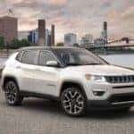 A white 2010 used Jeep Compass is parked on a pier in front of a river and city.