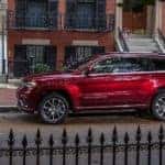 A red 2021 Jeep Grand Cherokee Summit is parked on the street behind a wrought iron fence.