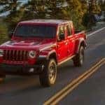 A red 2021 Jeep Gladiator Rubicon is driving down the road next to trees and a lake.