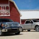 A dark blue and a silver 2014 used Ford F-150 Ranger XLT Lariat are parked in front of a red and white barn.