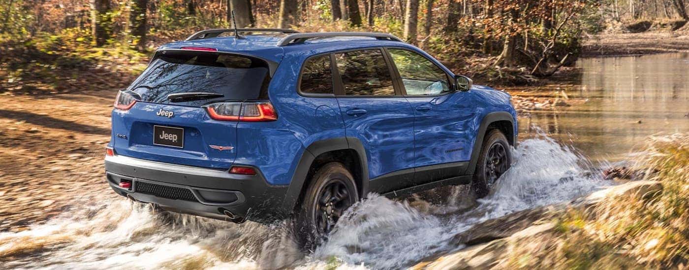 A blue 2021 Jeep Cherokee is off-roading in a river during a 2021 Jeep Cherokee vs 2021 Jeep Grand C…