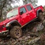 A red 2021 Jeep Gladiator with hard top is climbing over rocks after winning the 2021 Jeep Gladiator vs 2021 Ford Ranger comparison.