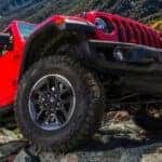A red 2019 Jeep Wrangler Unlimited is shown from a low angle climbing over rocks.