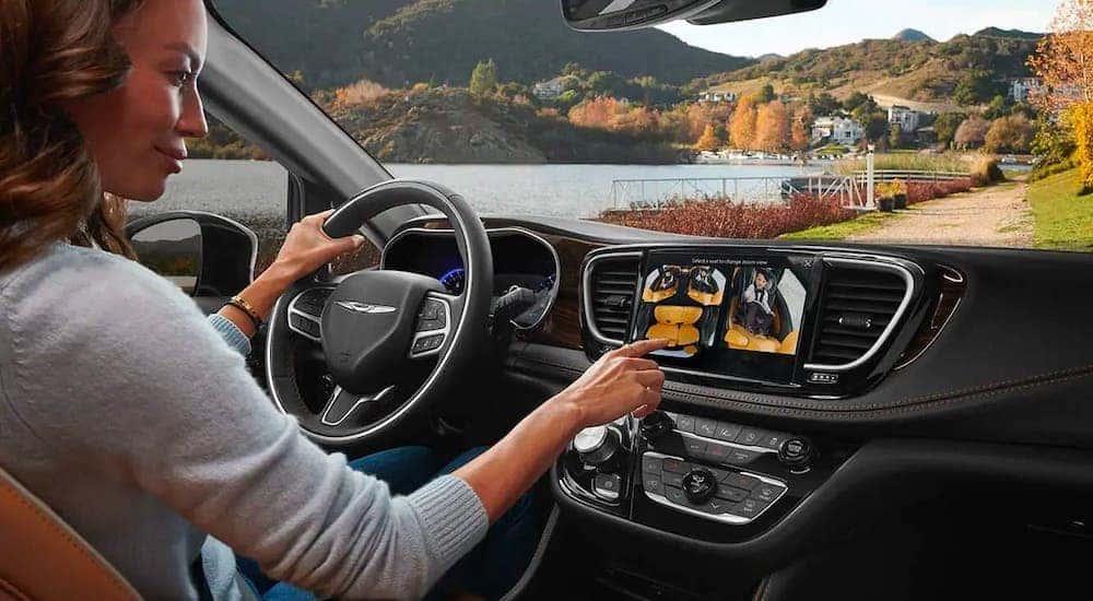 A woman in the driver's seat of a 2021 Chrysler Pacifica Hybrid is touching the infotainment screen using the FamCAM feature.