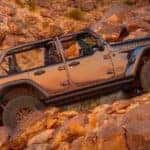 A silver 2021 Jeep Wrangler Rubicon 392 with no roof is shown from the side while climbing on a rocky road.