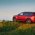 A red 2019 used Jeep Grand Cherokee is parked on a hill overlooking a coast.