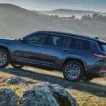 A black 2021 Jeep Grand Cherokee L is shown from the side driving on the side of a mountain trail after leaving a Black Forest Jeep dealer.