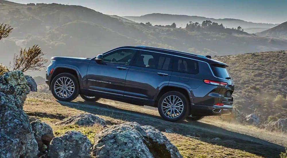 A black 2021 Jeep Grand Cherokee L is shown from the side driving on the side of a mountain trail after leaving a Black Forest Jeep dealer.