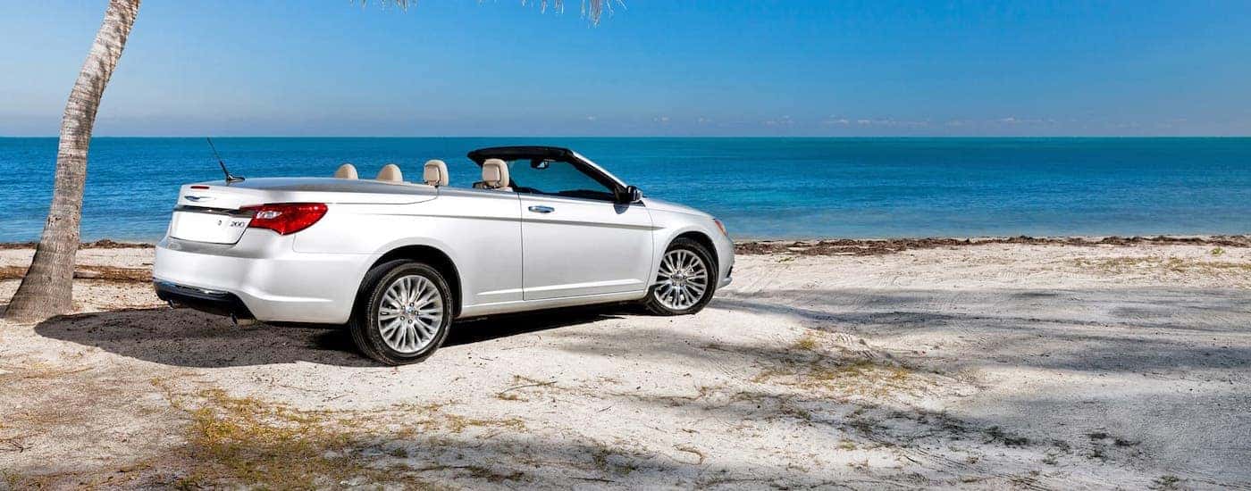 A white 2014 Chrysler 200 convertible is parked on a beach under a palm tree.