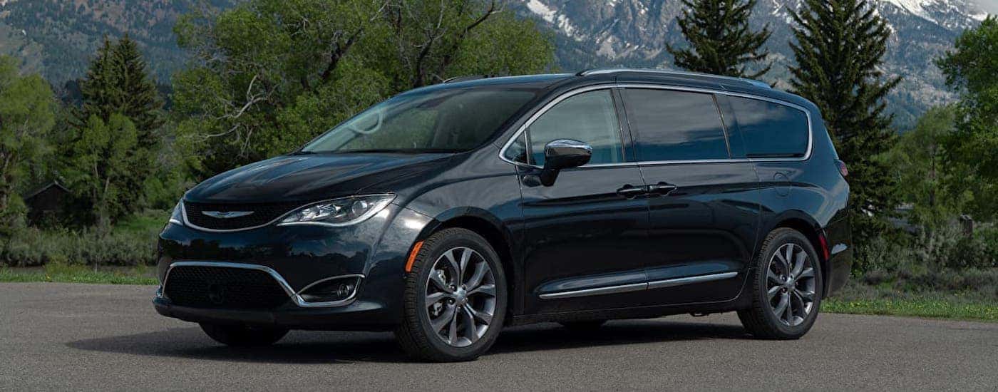 A black 2019 Chrysler Pacifica is parked in front of trees and mountains.