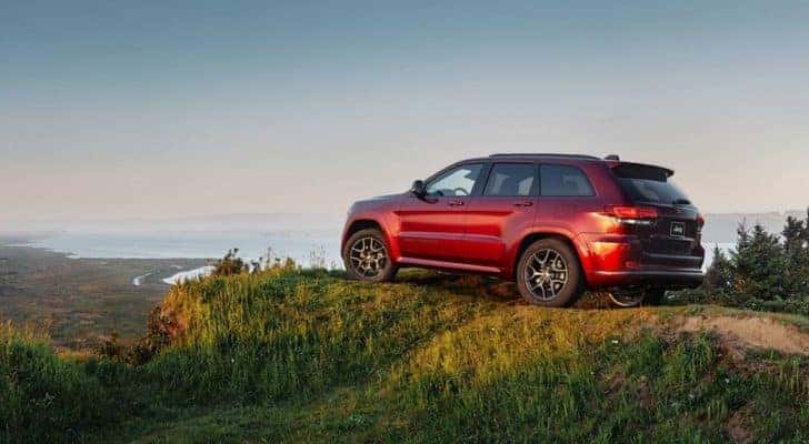 A red 2018 used Jeep Grand Cherokee is parked on a mountain overlooking the coast.