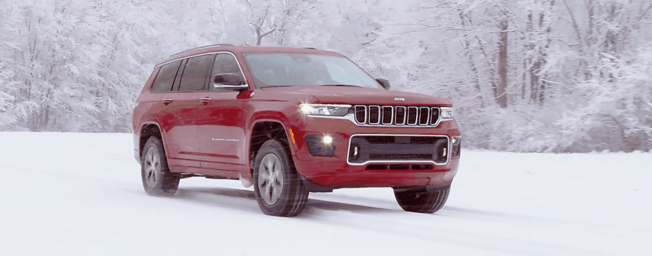A red 2021 Jeep Grand Cherokee L is driving on a road covered in snow.