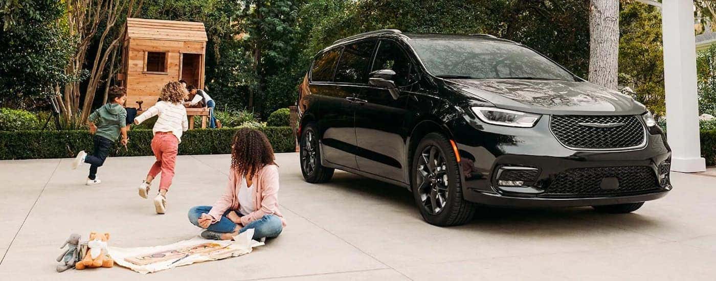 A family is playing in a driveway next to a black 2021 Chrysler Pacifica.