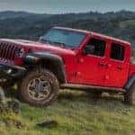 A red 2021 Jeep Gladiator Rubicon off-roading up a rocky green mountain