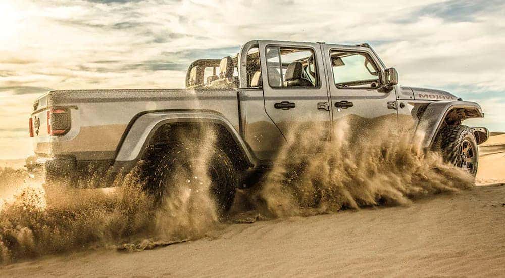 A silver 2021 Jeep Gladiator with no roof off-roading through desert sand.
