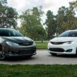 A white and a black 2020 Chrysler Pacifica are parked on a narrow road in front of a park.