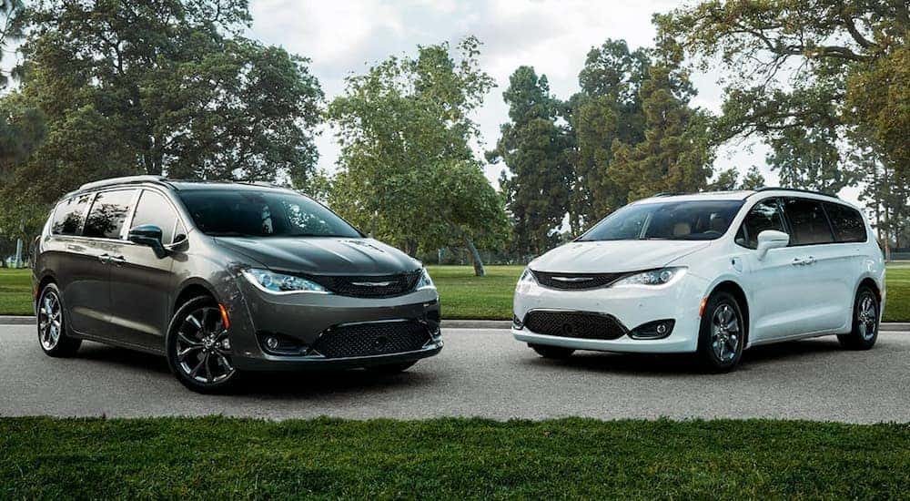 A white and a black 2020 Chrysler Pacifica are parked on a narrow road in front of a park.