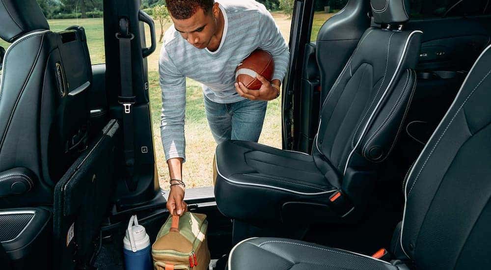 A person with a football is shown removing a bag from the interior of a 2021 Chrysler Pacifica Hybrid.