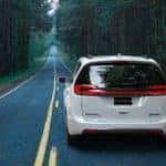 A white 2021 Chrysler Pacifica S Hybrid is shown from the rear driving down a wooded road after visiting a Chrysler Pacifica Hybrid dealer.