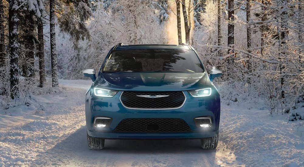 A blue 2020 Chrysler Pacifica Hybrid Pinnacle is shown from the front driving through a snowy forest.
