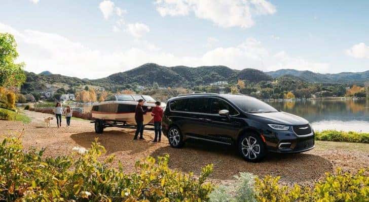 A black 2021 used Chrysler Pacifica Hybrid is towing a boat next to a lake.