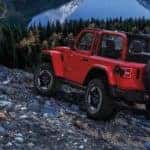 A red certified pre-owned Jeep Wrangler Rubicon parked on a rocky overlook above a lake